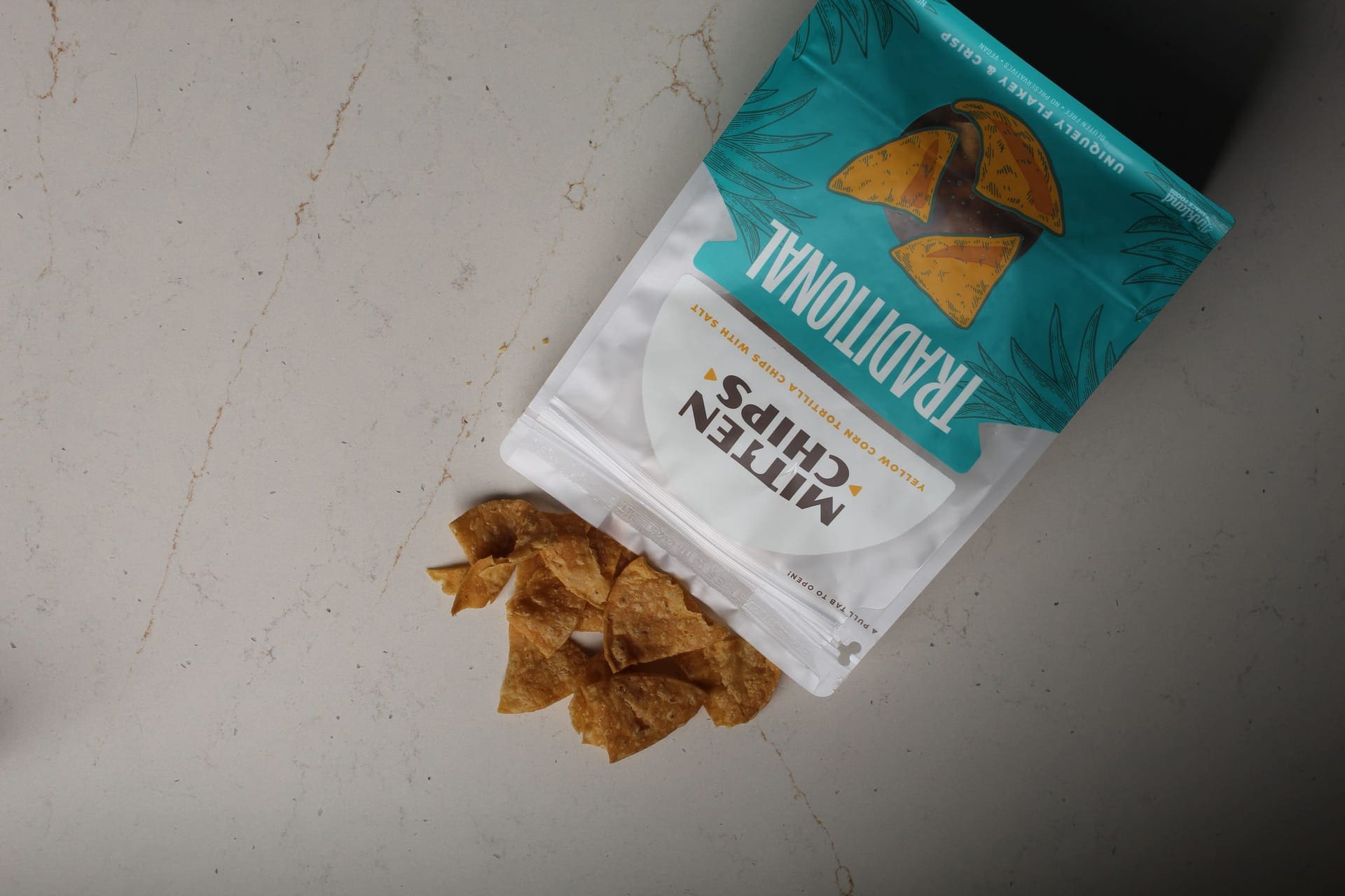 Mitten chips traditional chips on a marble table with the chips spilling out of the product bag